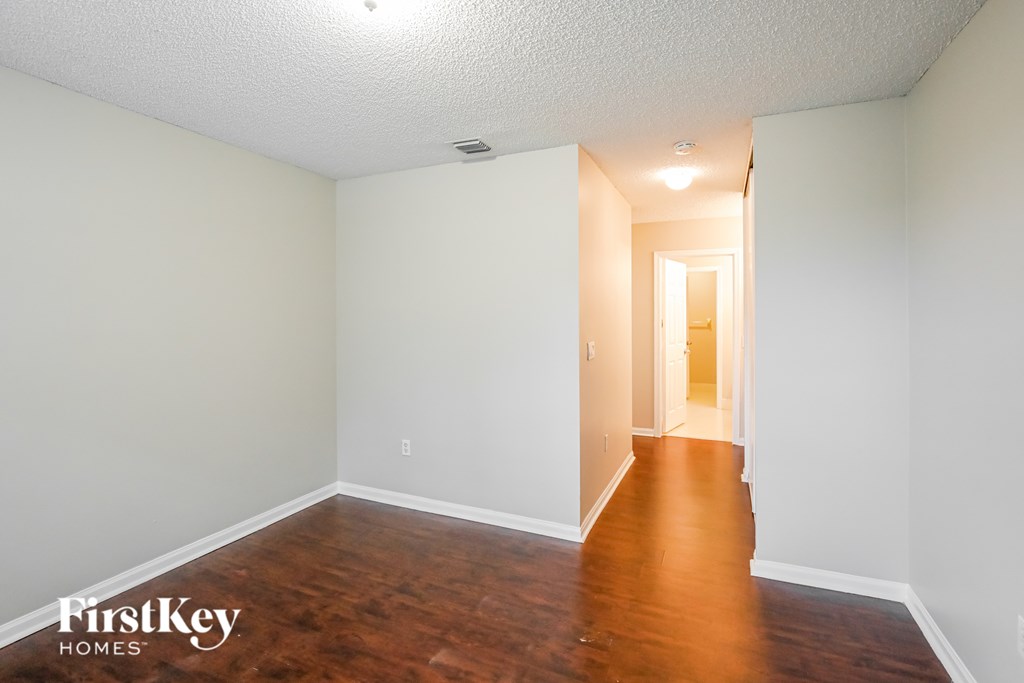 A room with wooden floors and white walls, with a doorway leading to another room.