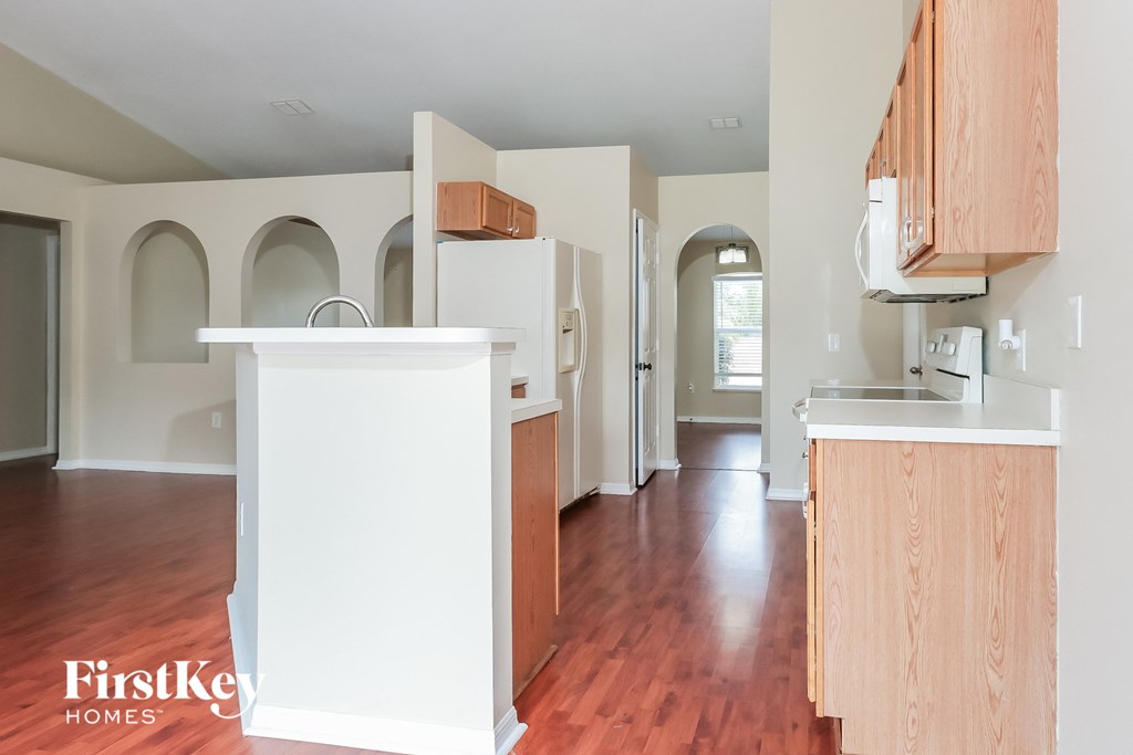 an empty kitchen with wood flooring and white cabinets and appliances