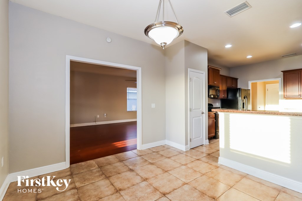 A spacious kitchen and living room with a tile floor and a hanging light fixture.
