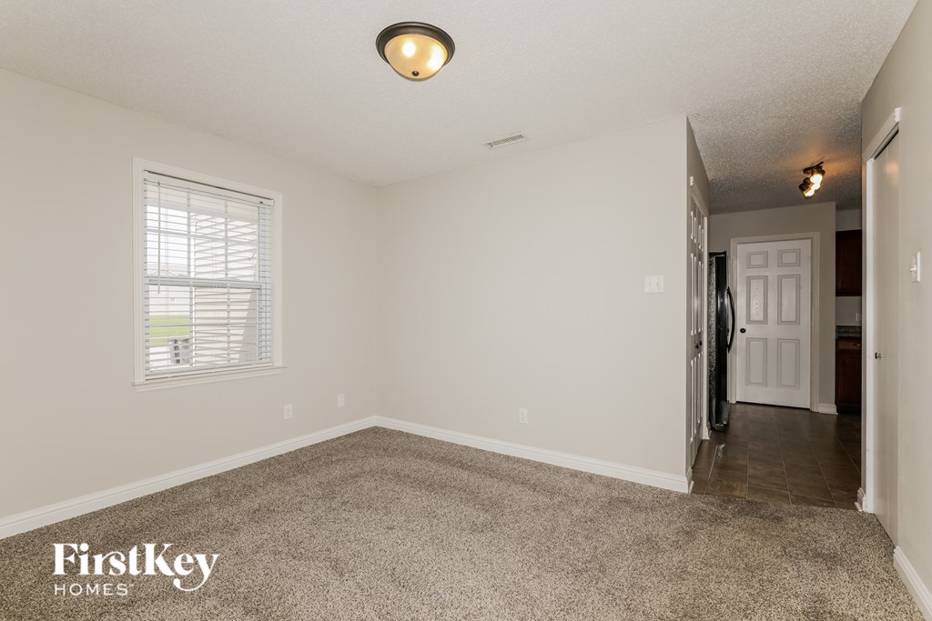 A room with a carpet floor, a window with blinds, a door, and a ceiling light.