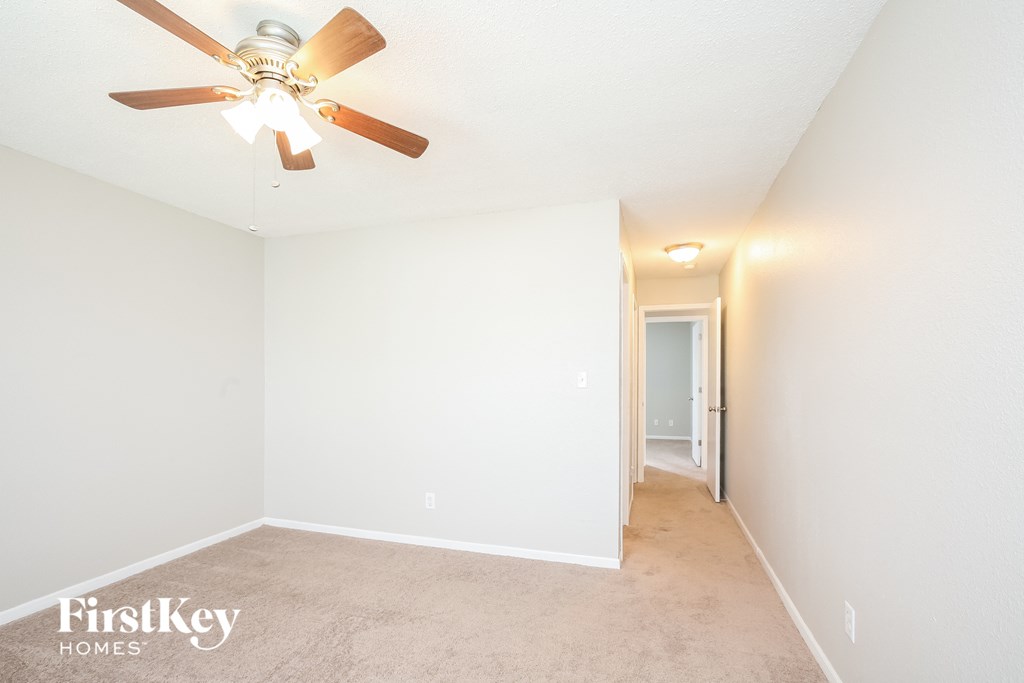a spacious living room with a ceiling fan and white walls