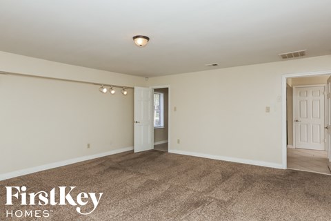 A spacious room with a carpeted floor and white walls, with a doorway leading to another room.