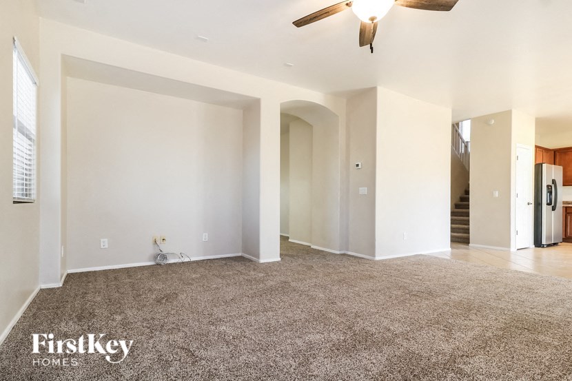 A spacious living room with a carpeted floor and a ceiling fan.