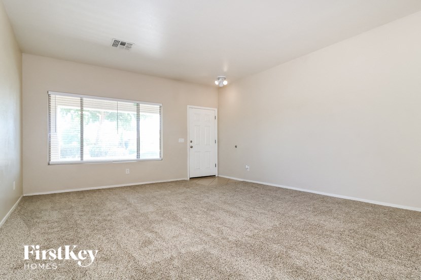A room with a carpeted floor, a window with blinds, a door, and a ceiling light fixture.