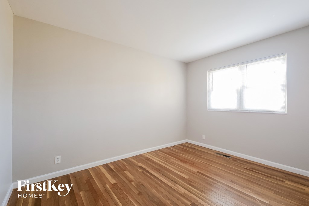 a bedroom with white walls and wood floors and a window
