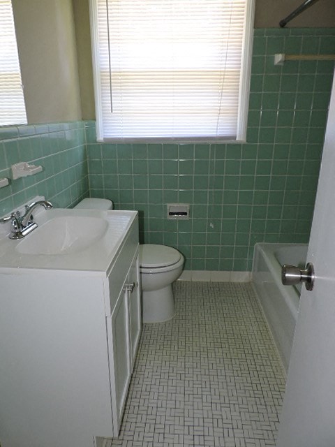 A white sink and toilet in a green tiled bathroom.