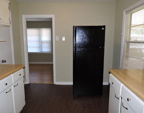 A black fridge stands in a kitchen with white cabinets and a wooden counter.