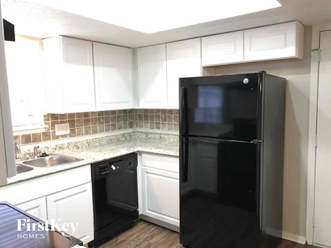 A black refrigerator stands in a kitchen with white cabinets and a tiled backsplash.