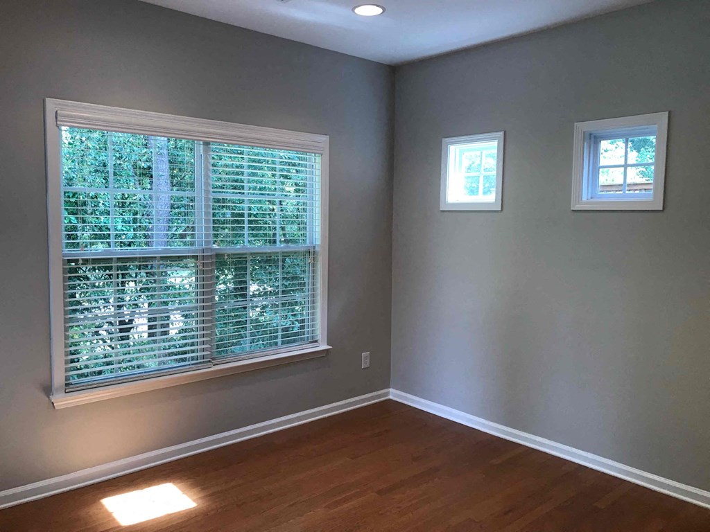 A room with a window covered in blinds and two small windows on the wall.