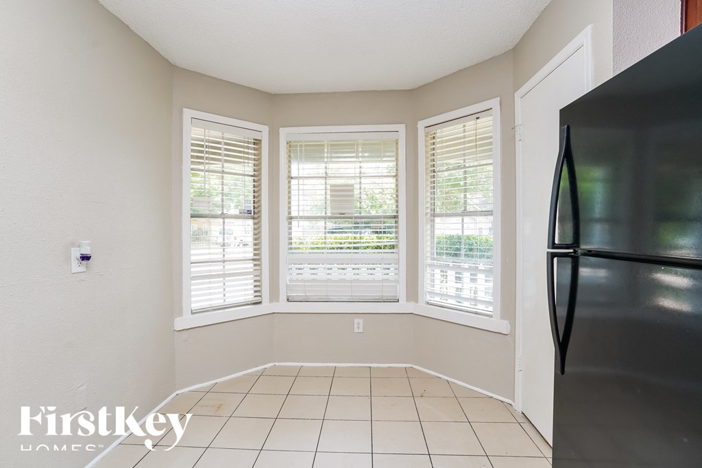 a small living room with three windows and a refrigerator