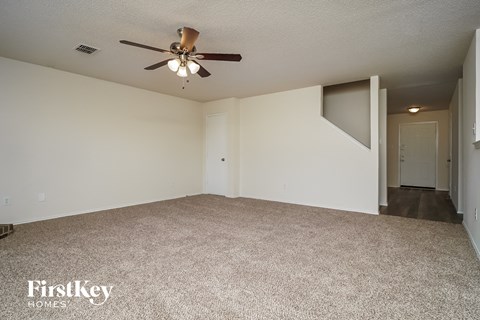 a spacious living room with carpet and a ceiling fan