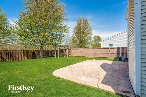 a backyard with a wooden fence and a patio with green grass and a house