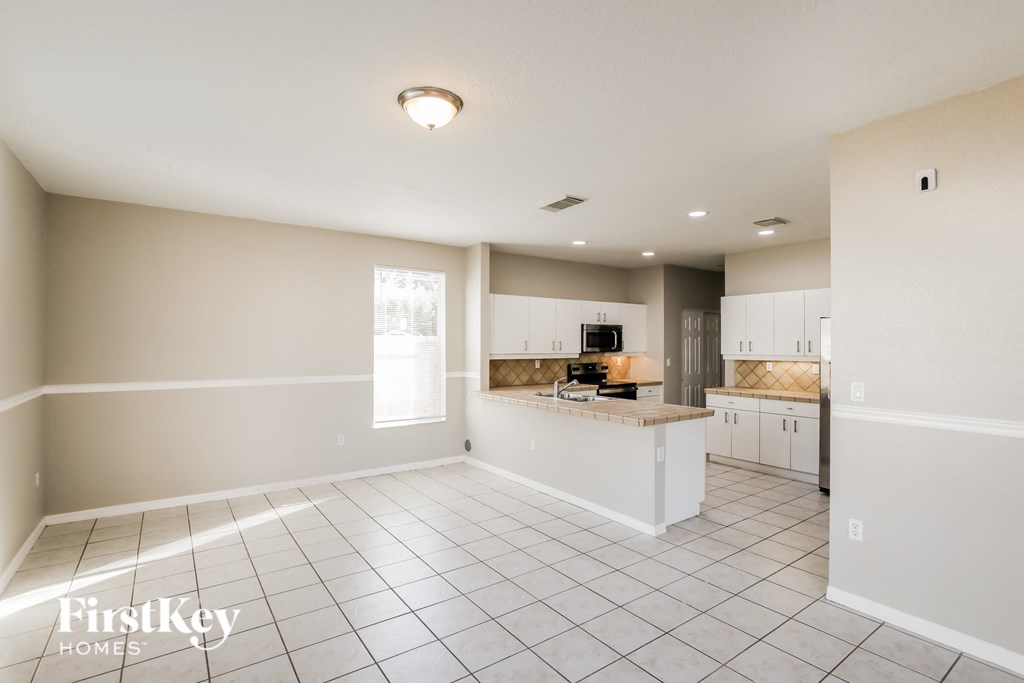 A spacious kitchen and living room with white tile flooring and a large island.