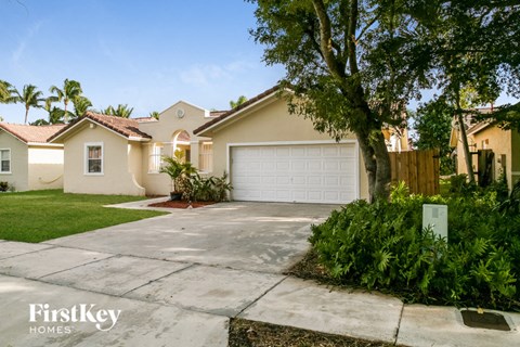 a beige house with a white garage door and a tree