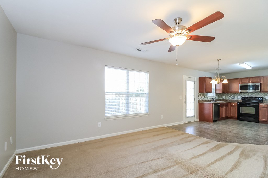 an empty living room with a ceiling fan and a kitchen