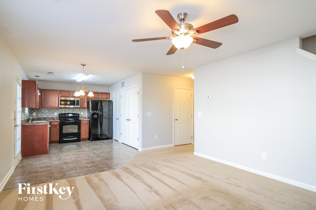 an empty living room with a ceiling fan and a kitchen
