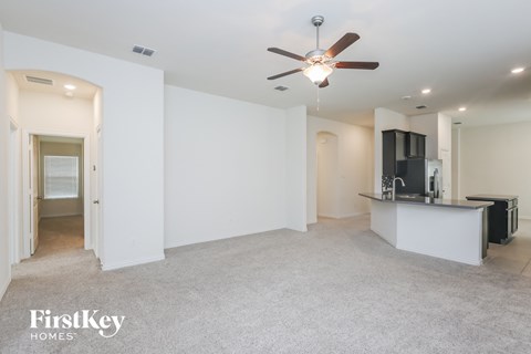 an empty living room with a kitchen and a ceiling fan