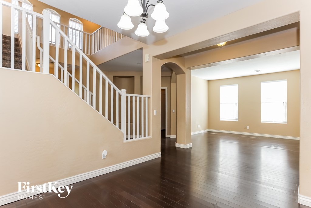 A spacious room with wooden floors and a staircase with white railings.