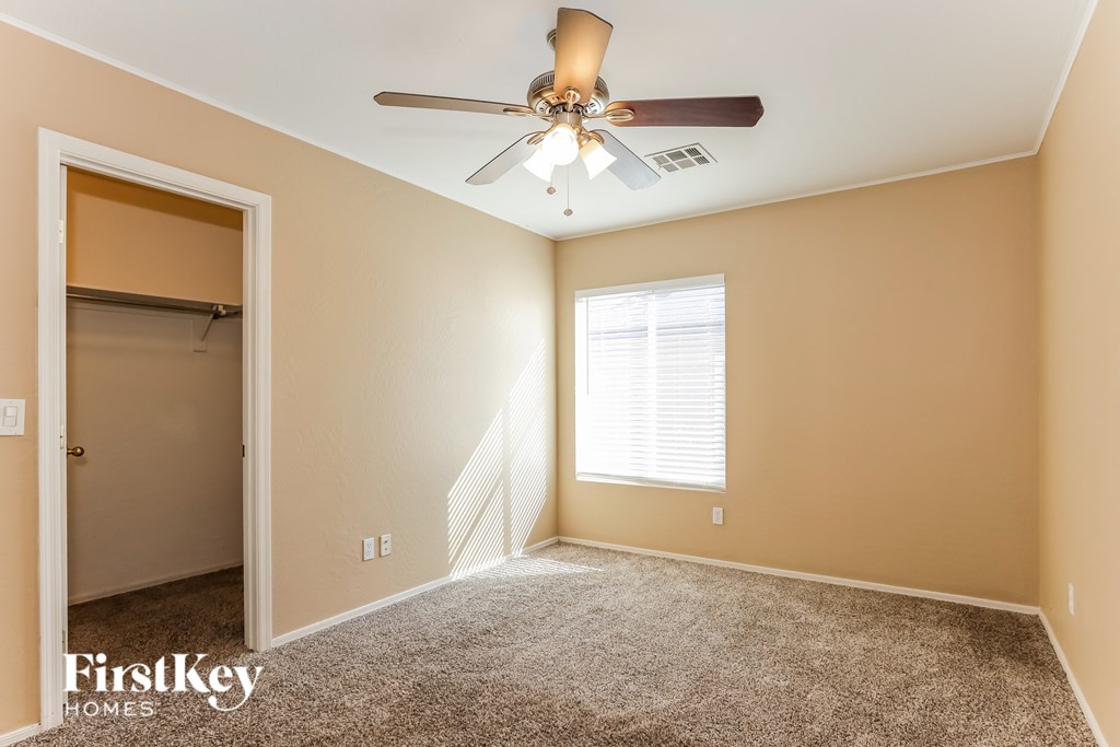 A room with a carpeted floor, a ceiling fan, and a window with blinds.