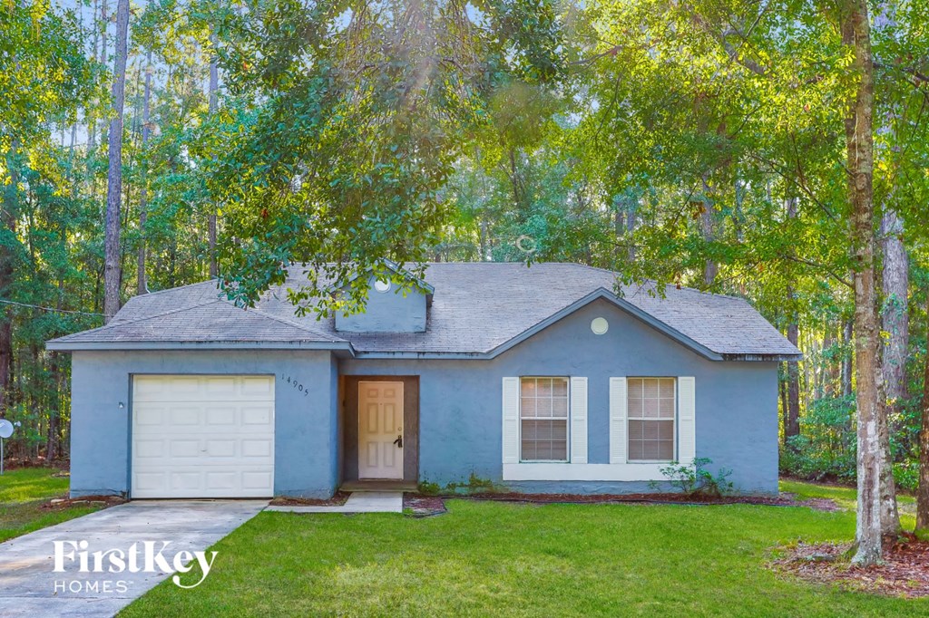A blue house with a white garage door is surrounded by trees.