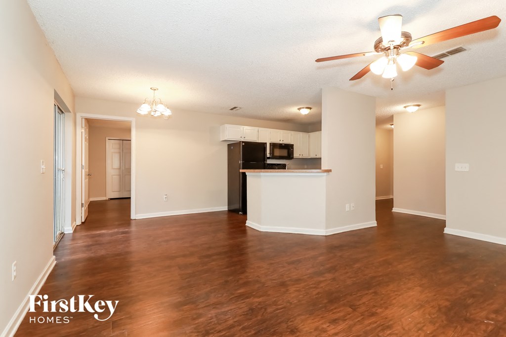 A spacious living room with a kitchen in the background and a ceiling fan above.
