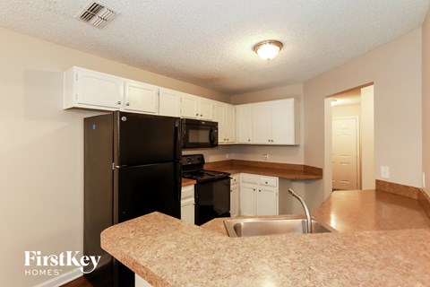 A kitchen with a black refrigerator and white cabinets.