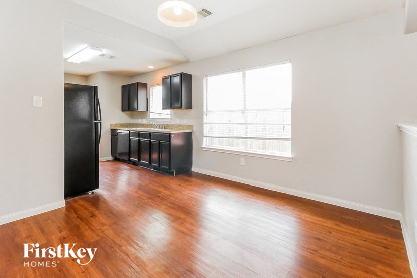 an empty living room and kitchen with wood floors and black appliances