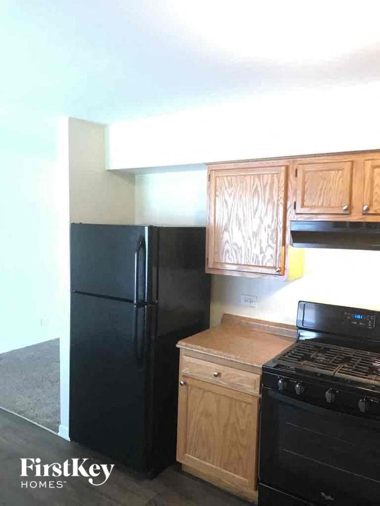 A black fridge and stove in a kitchen with wooden cabinets.