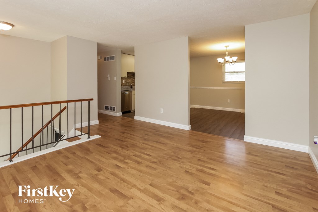 A spacious living room with wood flooring and a staircase with a railing.