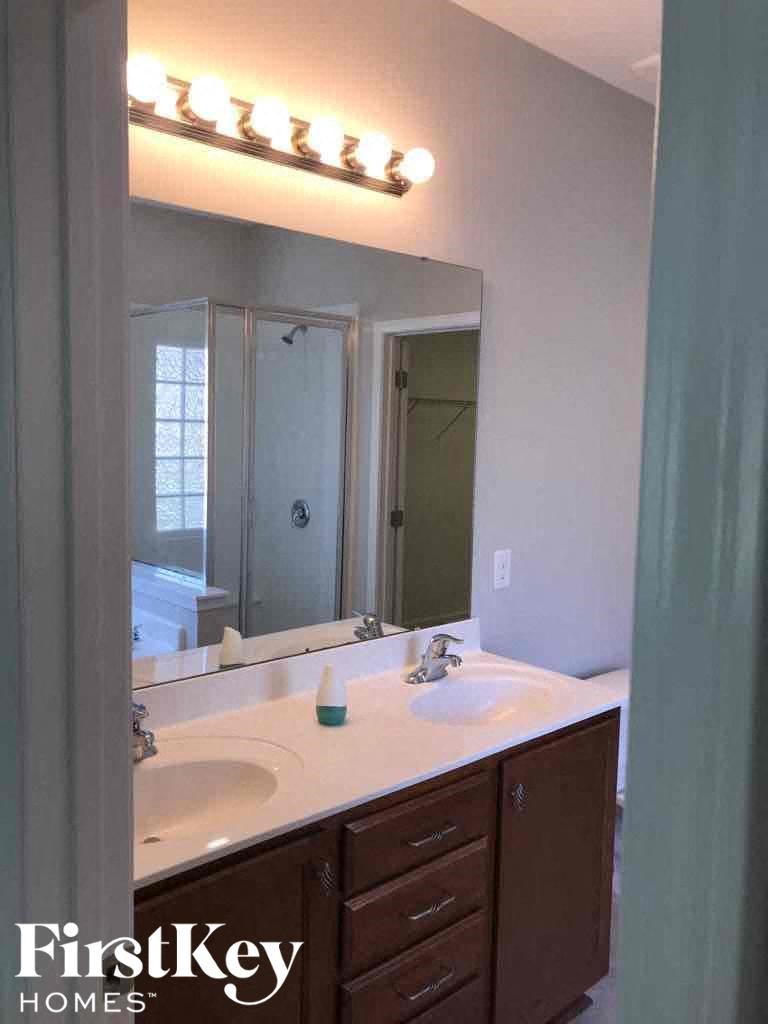 A bathroom with a white counter top and a mirror with lights above it.