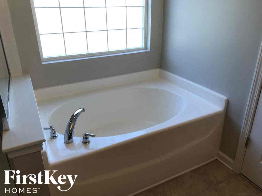 A white bathtub with a window above it in a bathroom.
