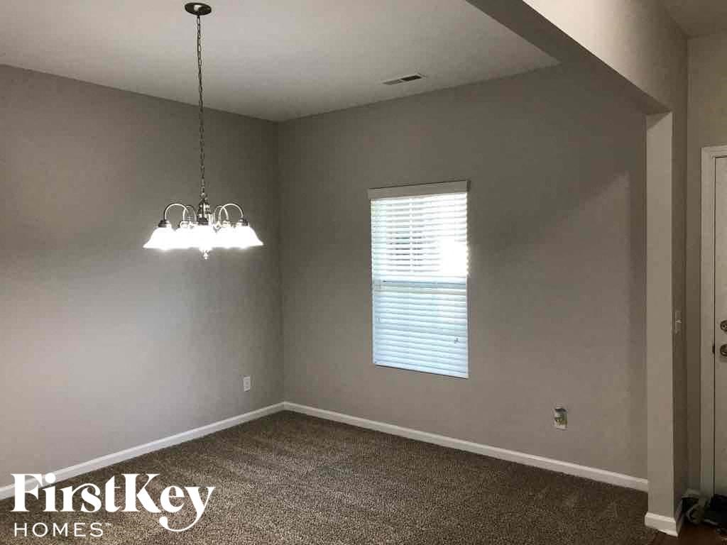 A room with a carpet floor, a chandelier, and a window with blinds.