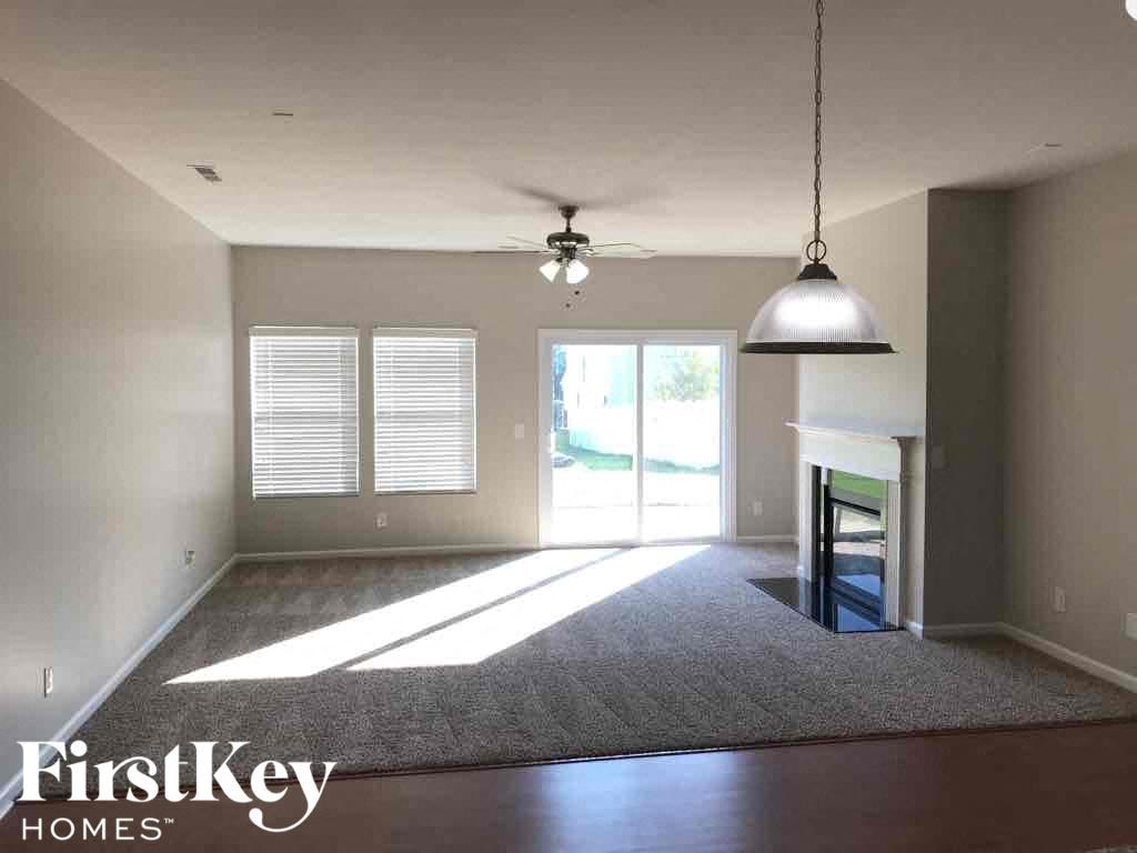 A spacious room with a rug, a ceiling fan, and a hanging light fixture.