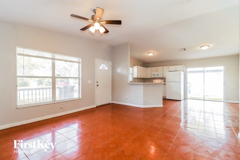 an empty living room with a kitchen and a ceiling fan