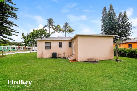 a small pink house with a grass yard and palm trees