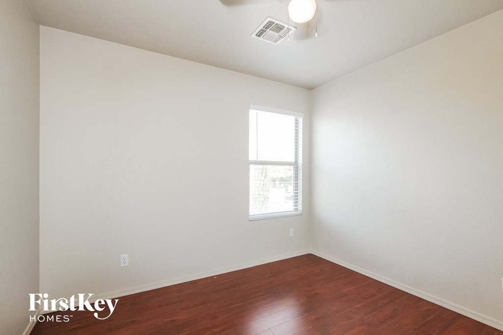 a bedroom with white walls and wood floors and a window