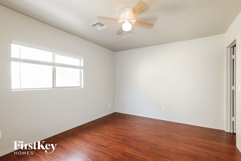 a bedroom with white walls and wood floors and a ceiling fan
