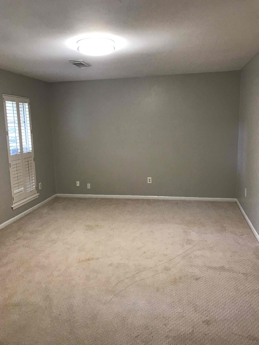 A room with a carpeted floor and a window with blinds.