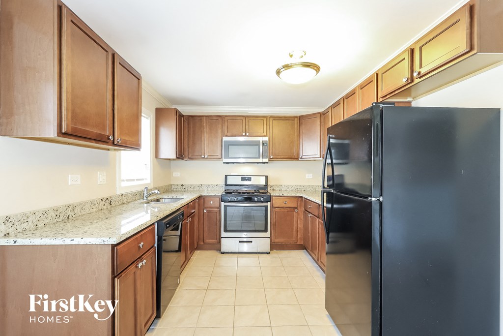 A kitchen with a black refrigerator, brown cabinets, and a granite countertop.