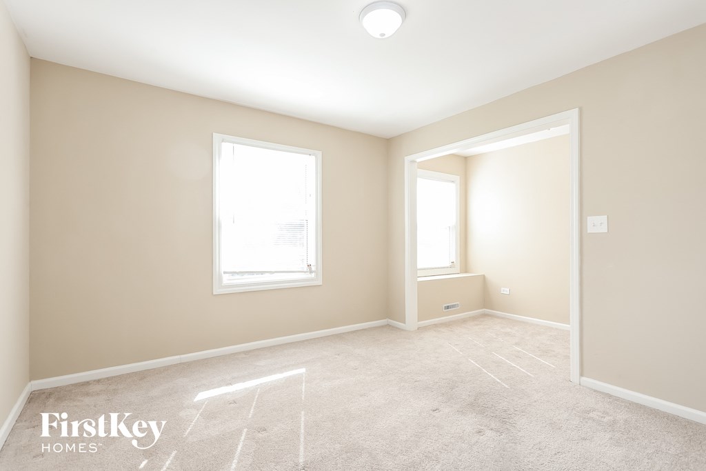 A spacious room with a carpeted floor and two windows.