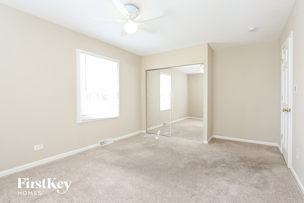 A room with a carpet floor, a ceiling fan, and a large mirror.