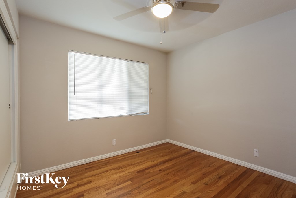 a bedroom with wood flooring and a window and a ceiling fan