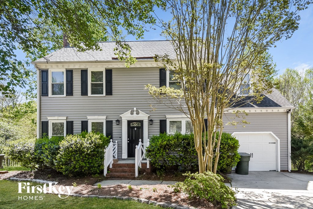 A house with a grey facade and a black door is surrounded by greenery.