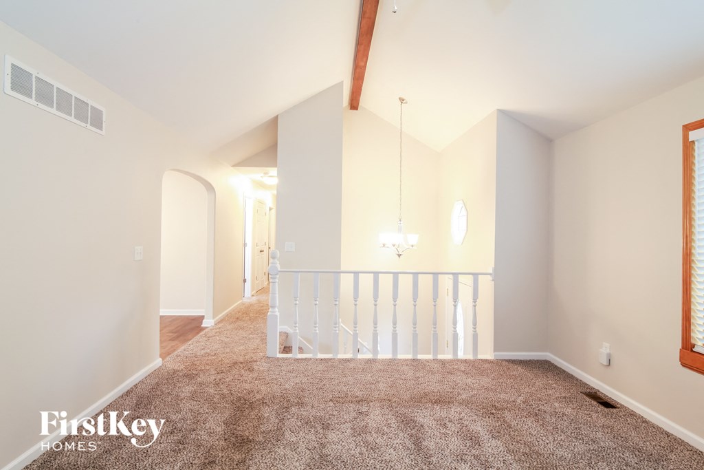 A spacious room with a carpeted floor and a balcony with white railings.