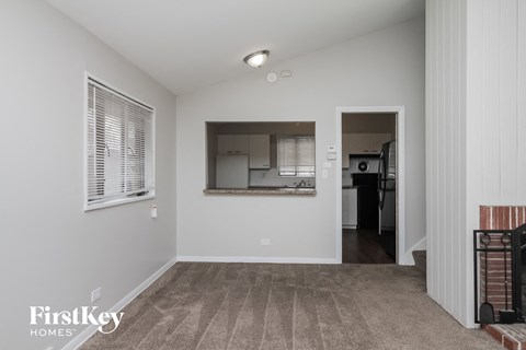 an empty living room with a kitchen in the background