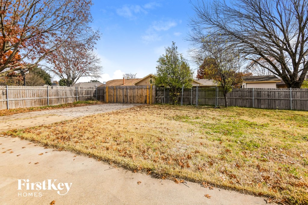 A fenced backyard with a grassy area and trees.