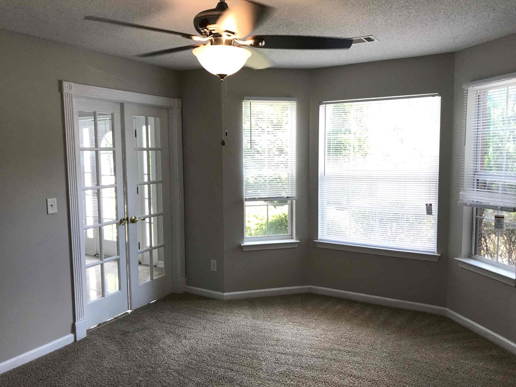 an empty living room with a ceiling fan and three windows