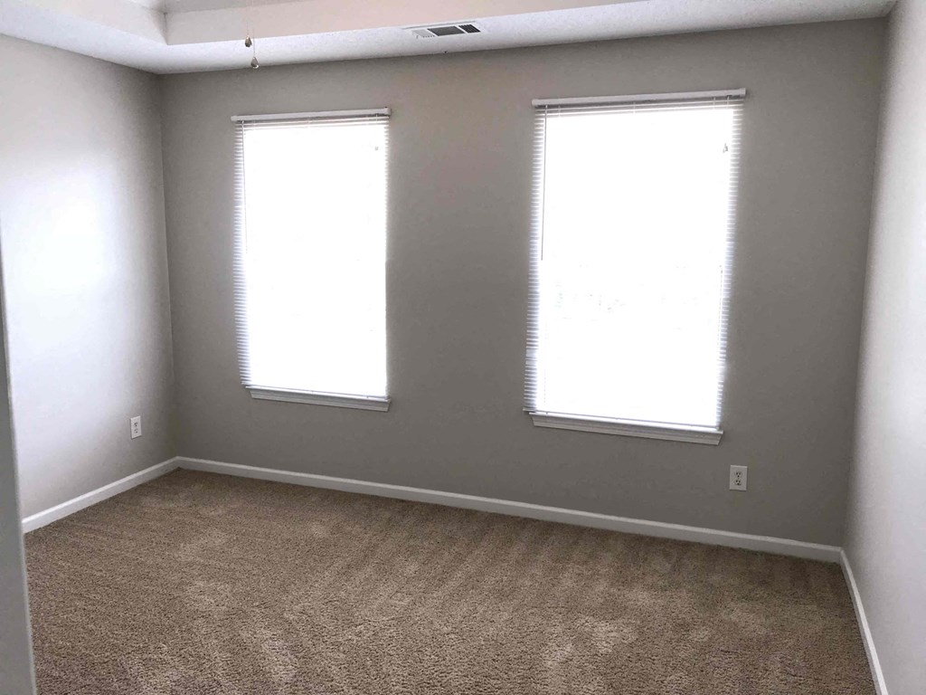 an empty room with two windows and a carpet
