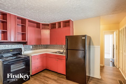 A kitchen with red cabinets and a black refrigerator.