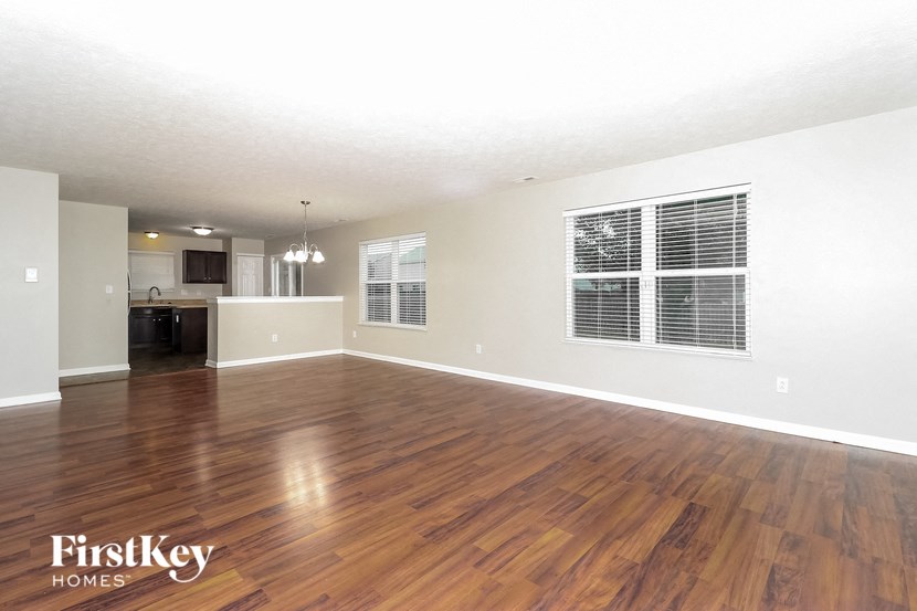 an empty living room with wood flooring and a kitchen